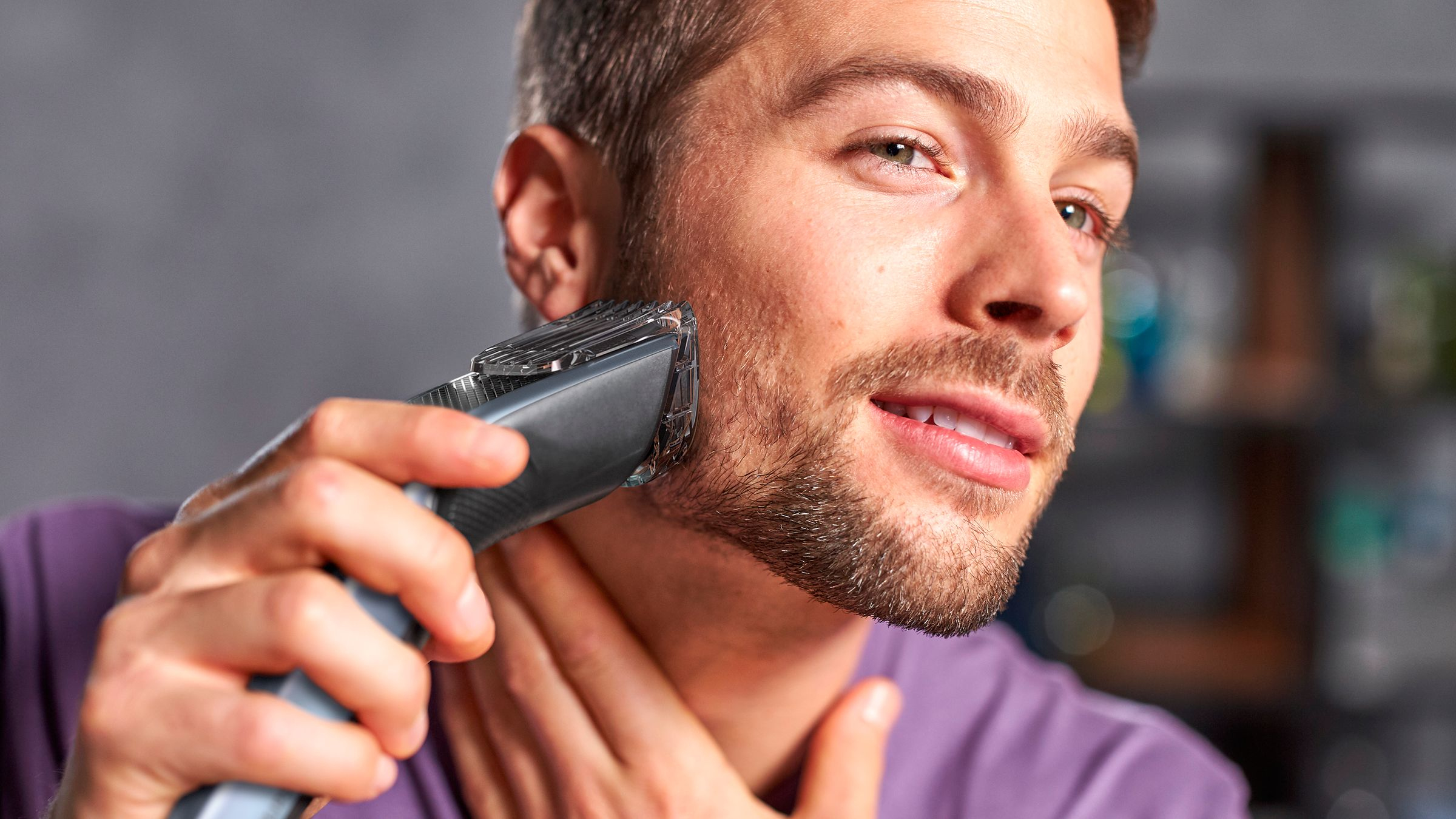 Un hombre se está recortando la barba con una recortadora. Mira hacia la derecha.