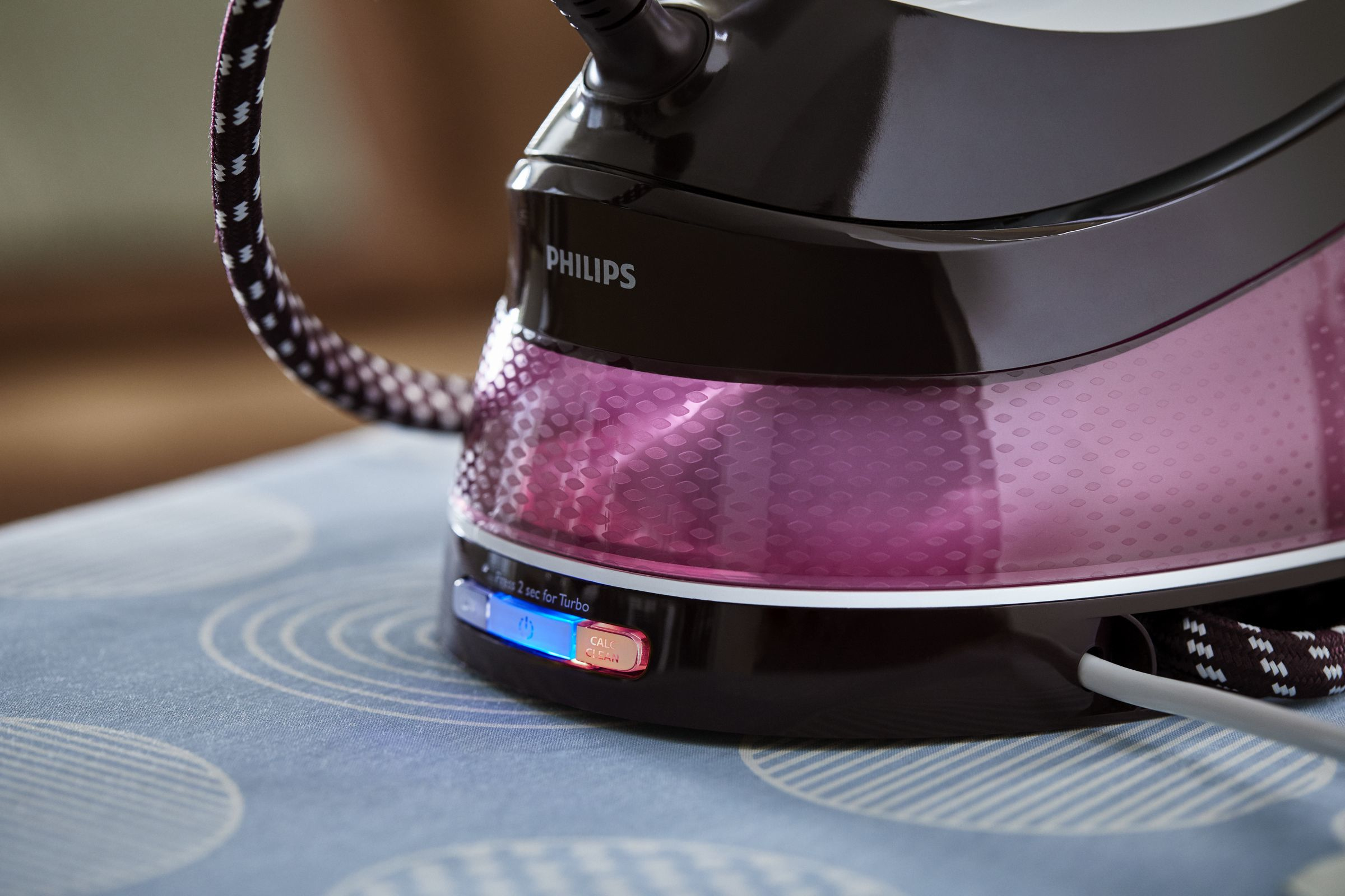 Una plancha de vapor Philips negra y morada sobre una tabla de planchar azul estampada.