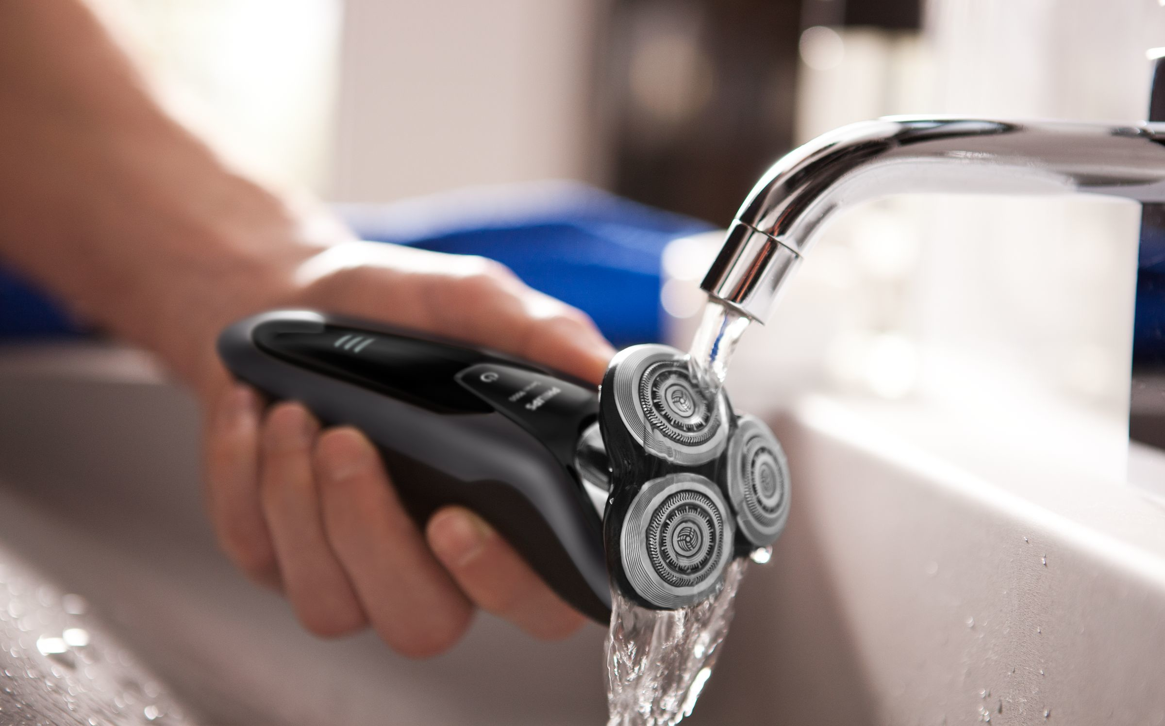 Una persona sostiene una afeitadora negra bajo el agua corriente en un lavabo.