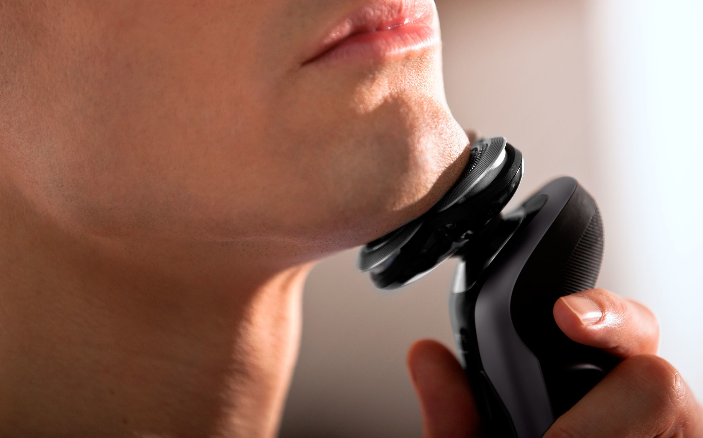 Primer plano de un hombre afeitándose el cuello con una afeitadora eléctrica negra. La afeitadora está en uso.