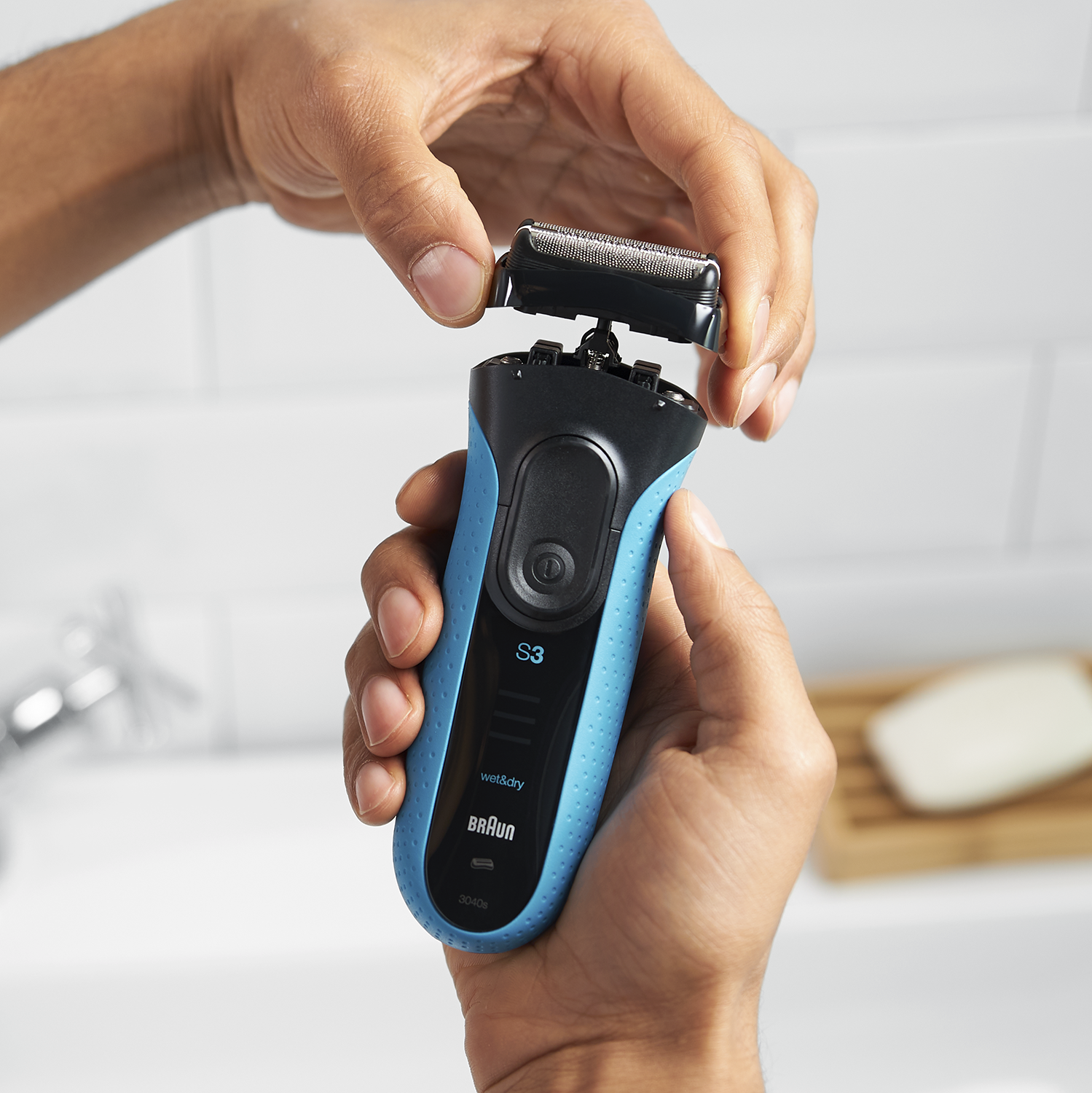 A person holding a blue and black Braun electric shaver, showing the head.