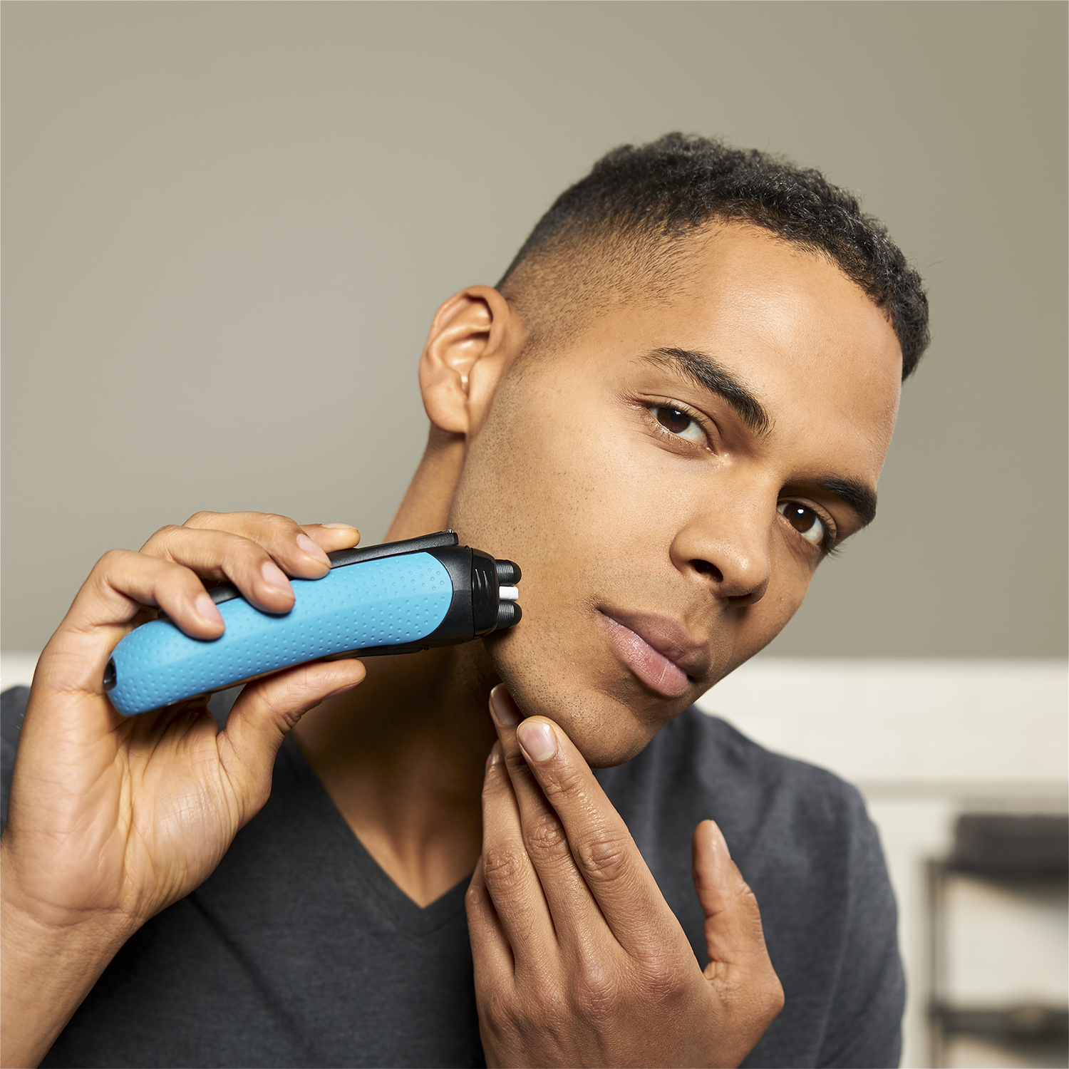A black man shaves his face with a blue and black electric shaver.