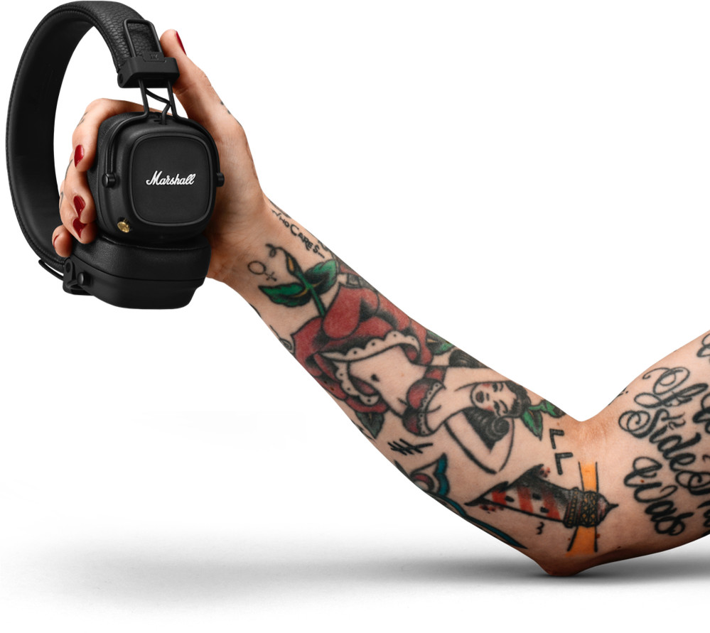 A person's arm with tattoos holding black Marshall headphones. White background.