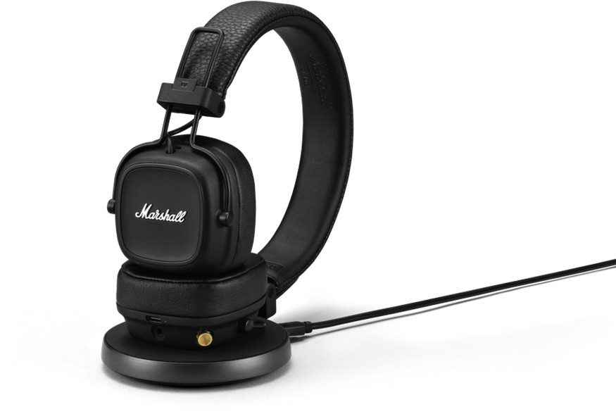 Black headphones on a charging stand, with a charging cable.