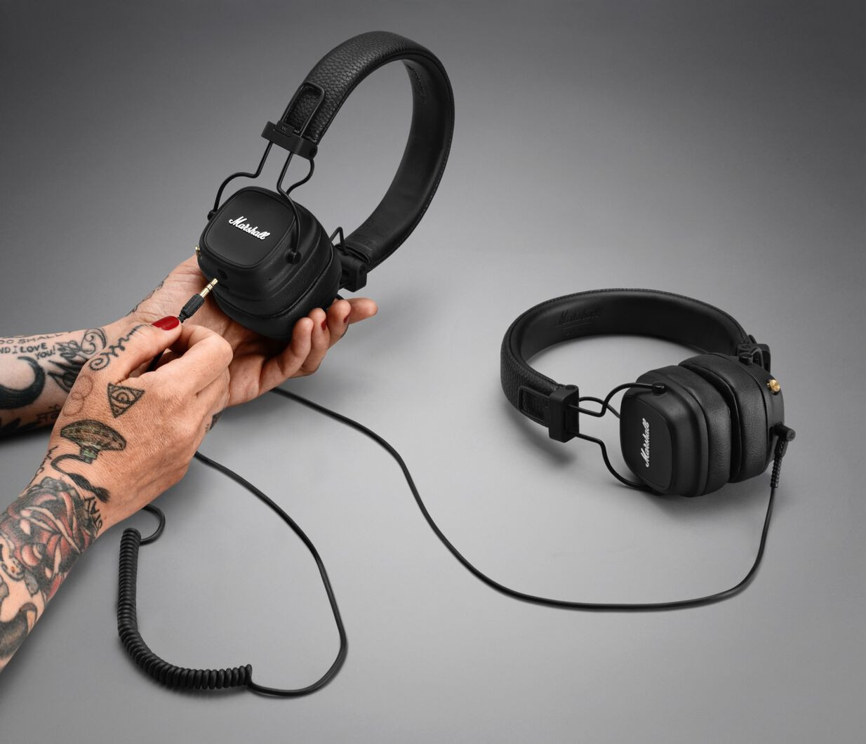 Black headphones with Marshall logo, plugged into a hand with tattoos.