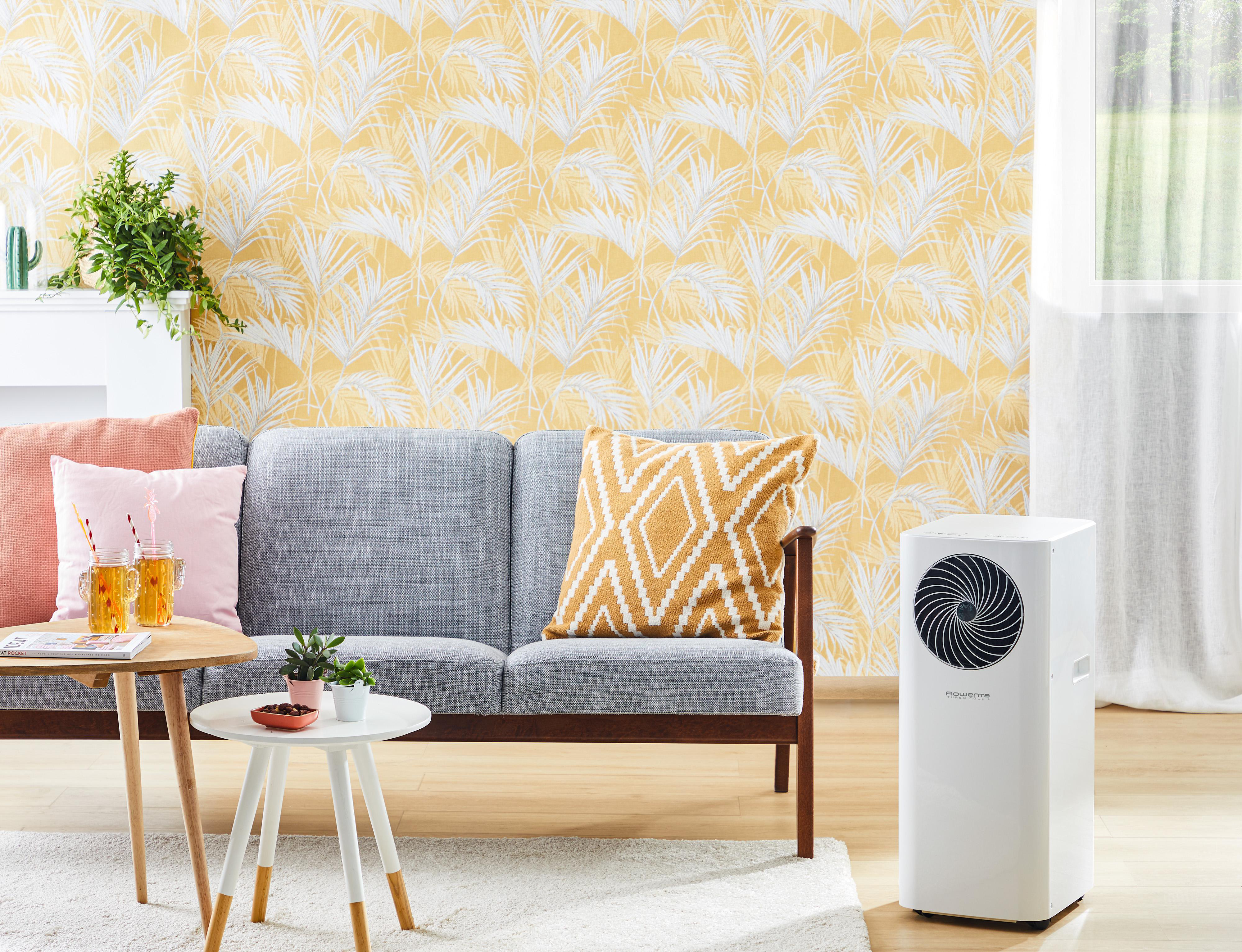 Wohnzimmer mit grauem Sofa, gelber Tapete, Klimaanlage und kleinen Tischen.