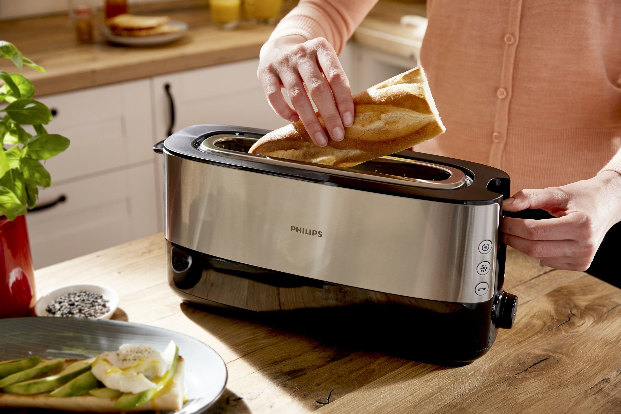 Persona insertando pan en una tostadora Philips en una mesa de madera.