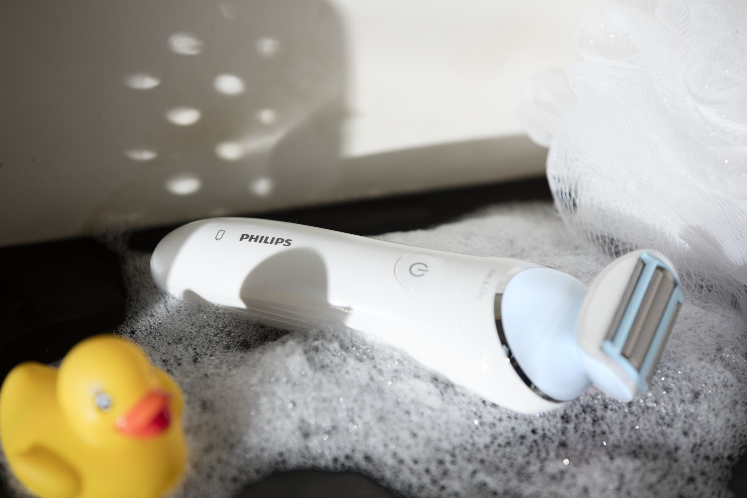 Una afeitadora Philips blanca en un lavabo con burbujas y un patito de goma.