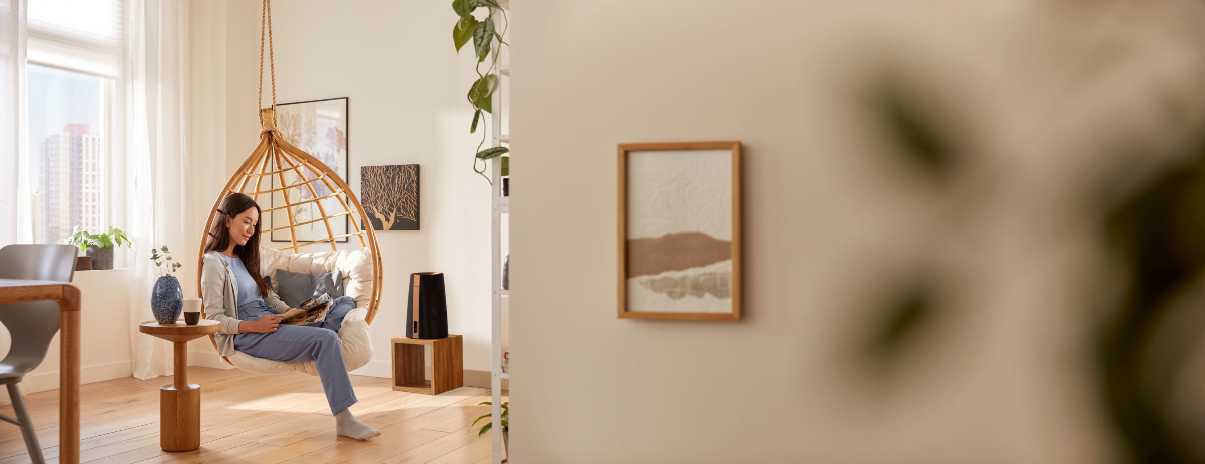 Frau liest in einem Hängesessel. Der Raum hat Kunst und Pflanzen. Auf einem Holzständer ein Lautsprecher.