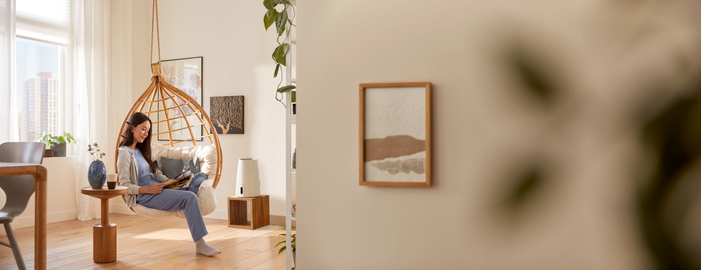 Eine Frau liest in einem Hängesessel in einem Wohnzimmer mit Holztisch und Pflanzen.