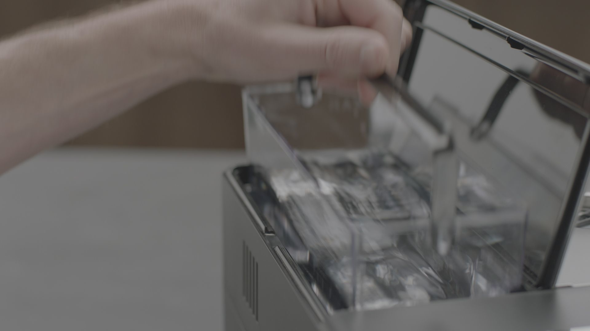 Una mano abriendo un compartimento de una máquina para revelar contenedores transparentes con elementos dentro.