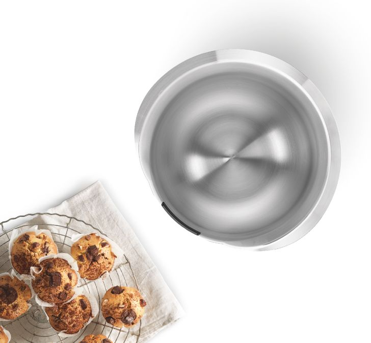 Muffinok drótrácson, egy rozsdamentes acél tál mellett. Fehér háttér.