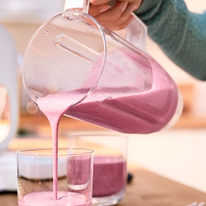 Rózsaszín turmixot öntenek átlátszó turmixgépből egy pohárba. Egy második pohárban van egy kis turmix.