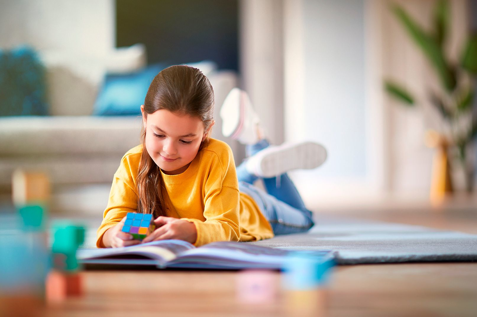Genç bir kız kitap okuyor ve bir Rubik küpüyle oynuyor.