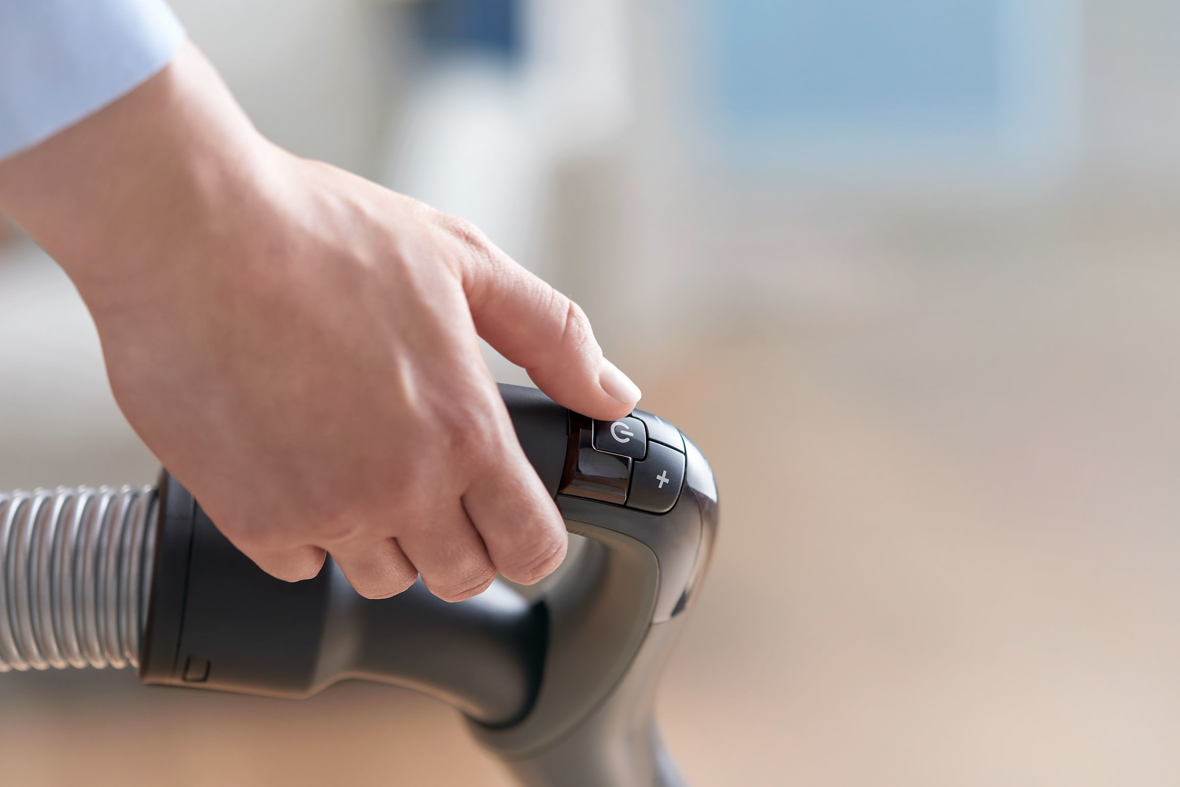 Üzerinde güç ve artı düğmeleri bulunan bir elektrikli süpürge sapını tutan bir el.