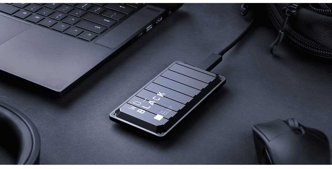 Disque dur externe noir connecté à un ordinateur portable sur un bureau avec un casque.