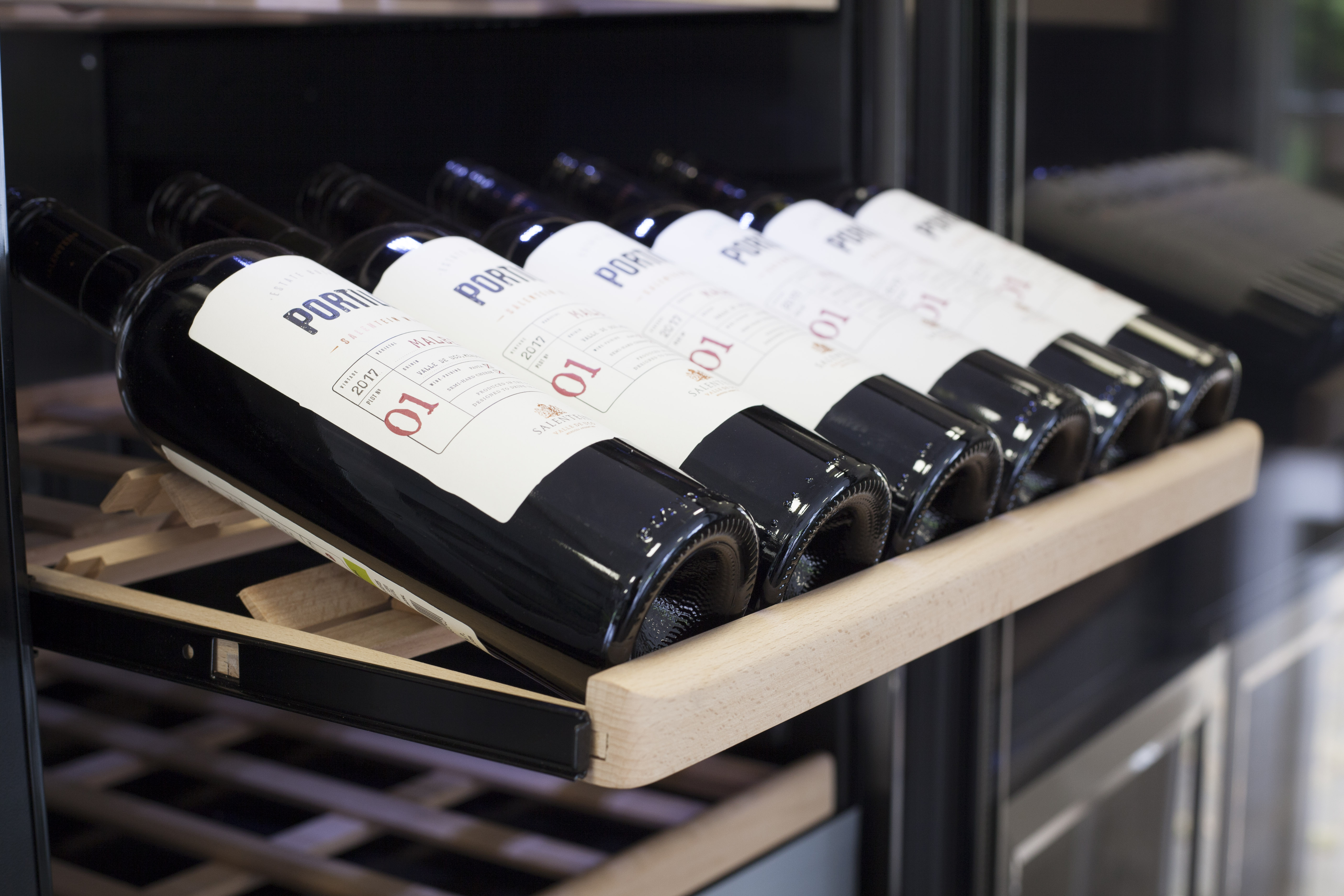 Flaschen Rotwein auf einem Holzregal in einem Weinkühlschrank.