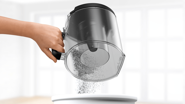 Die Hand einer Person gießt Staub aus einem Staubsaugerbehälter aus.