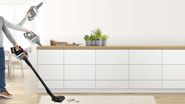 Eine Person benutzt einen Bosch Staubsauger in einer Küche. Der Staubsauger zeigt Zubehör.