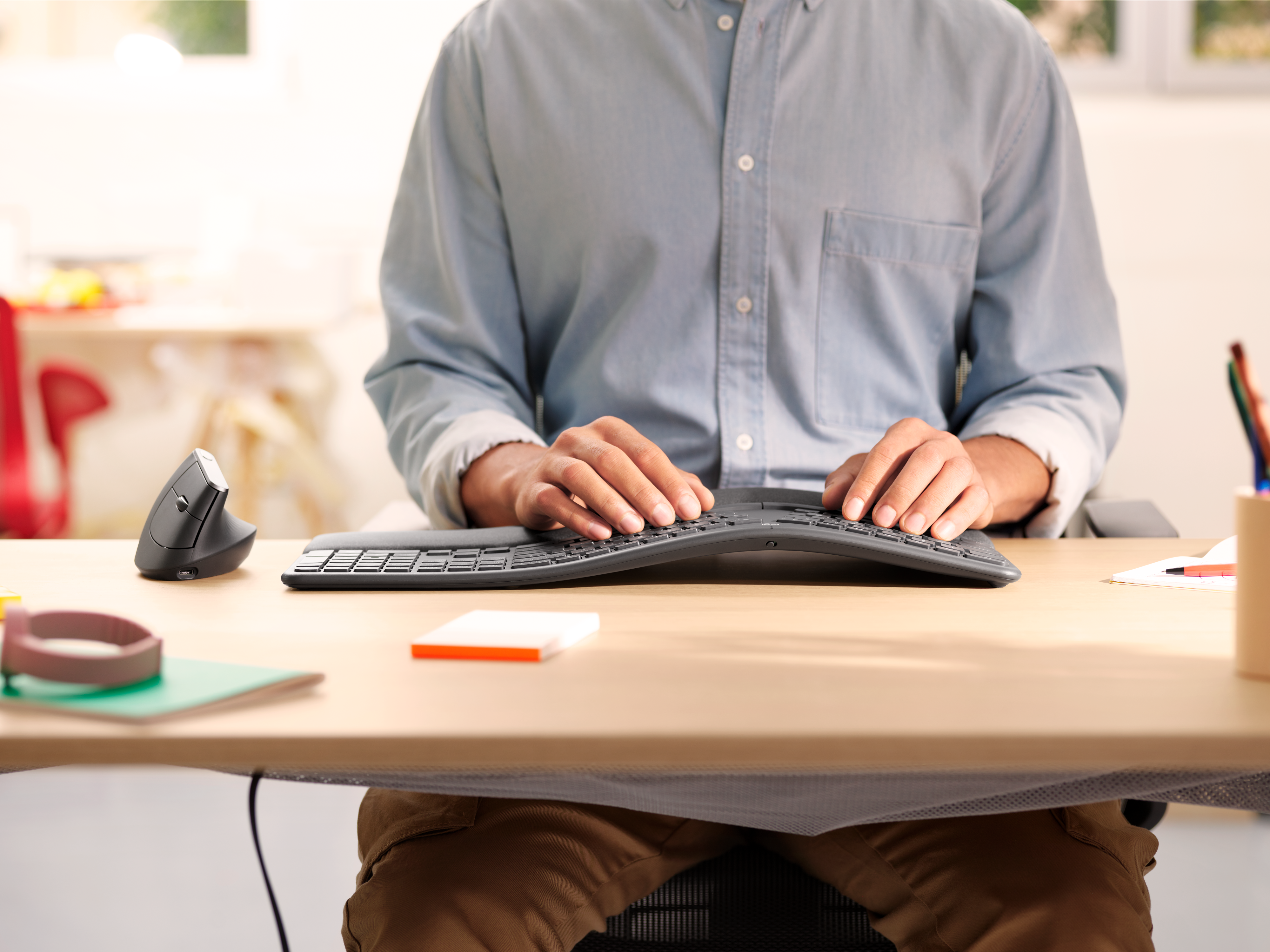 Una persona digita su una tastiera curva su una scrivania con un mouse e altri oggetti.
