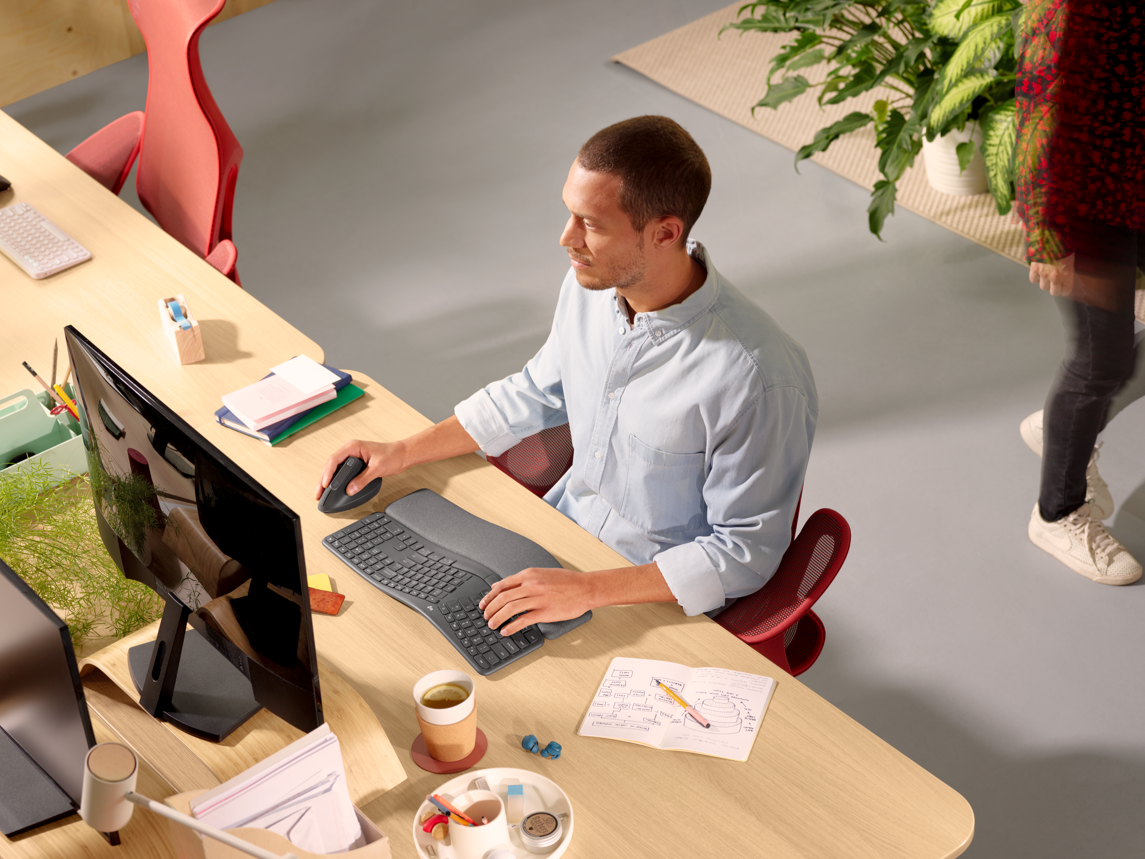 Una persona che lavora a una scrivania con tastiera, mouse e monitor. C'è una sedia rossa.