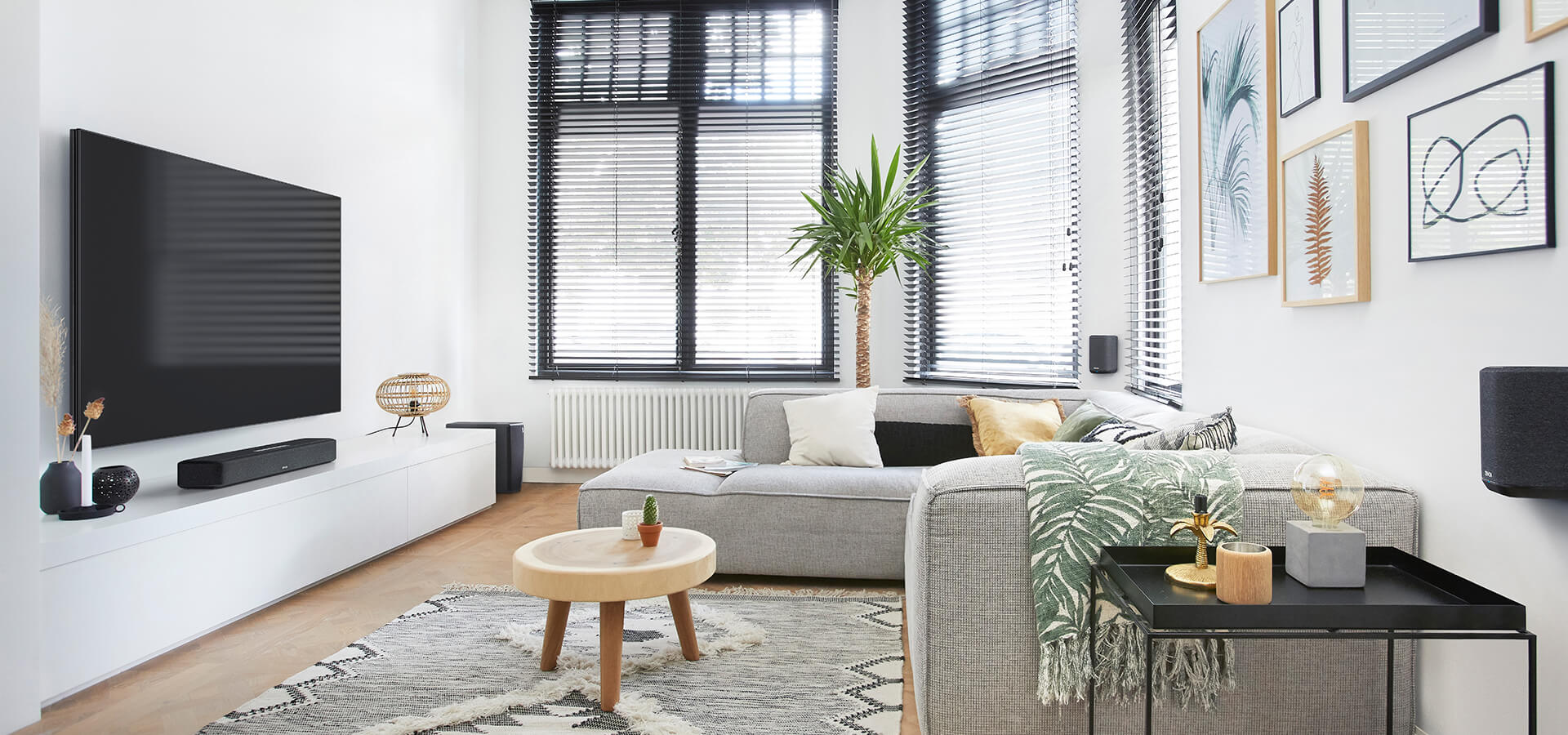 Wohnzimmer mit großem Fernseher, Sofa und diverser Einrichtung. Fenster und Tageslicht vorhanden.