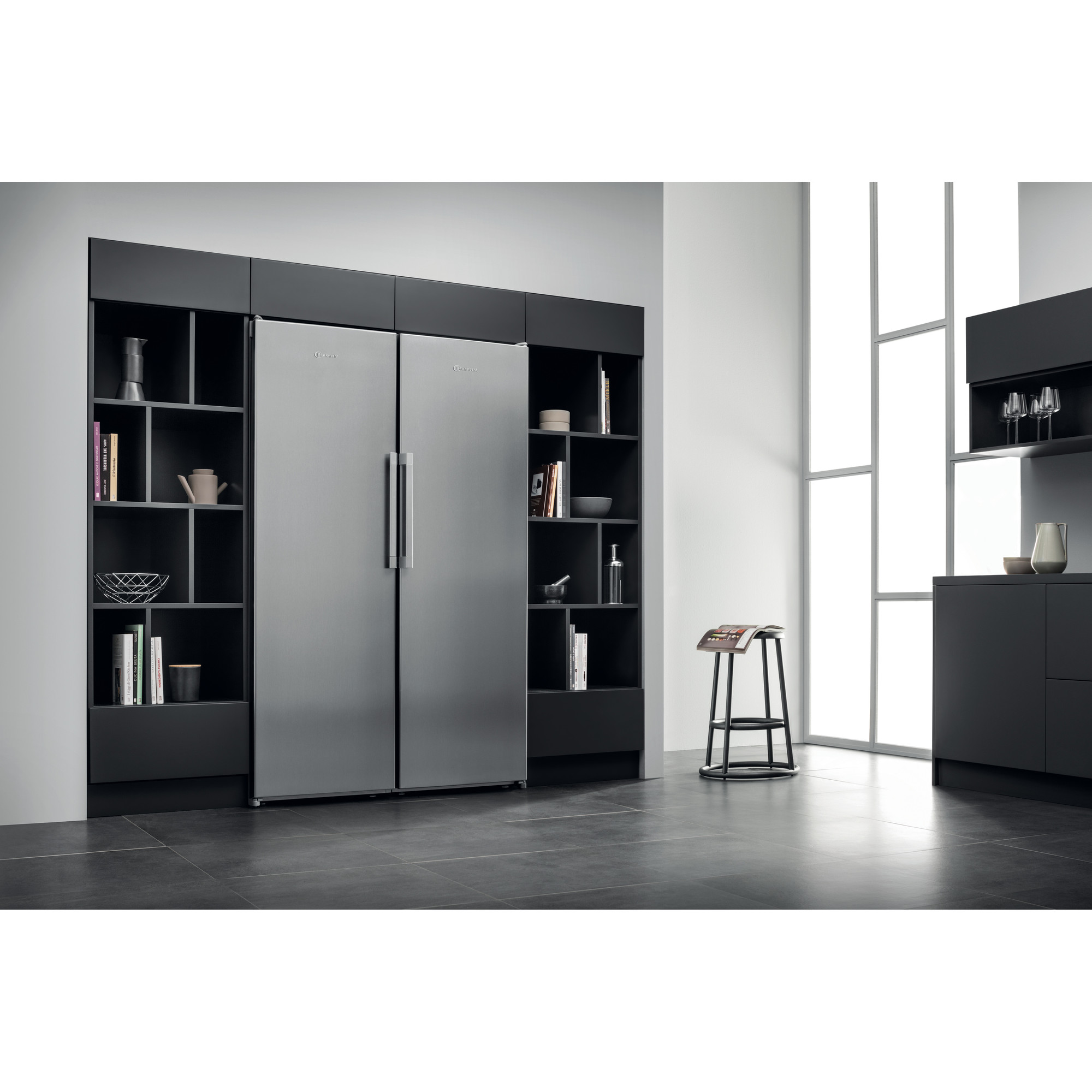 Edelstahlkühlschrank neben schwarzen Regaleinheiten und einem Hocker.