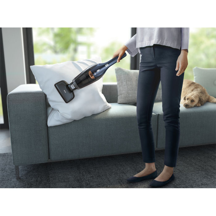 Eine Frau saugt mit einem Handstaubsauger ein Sofa ab.