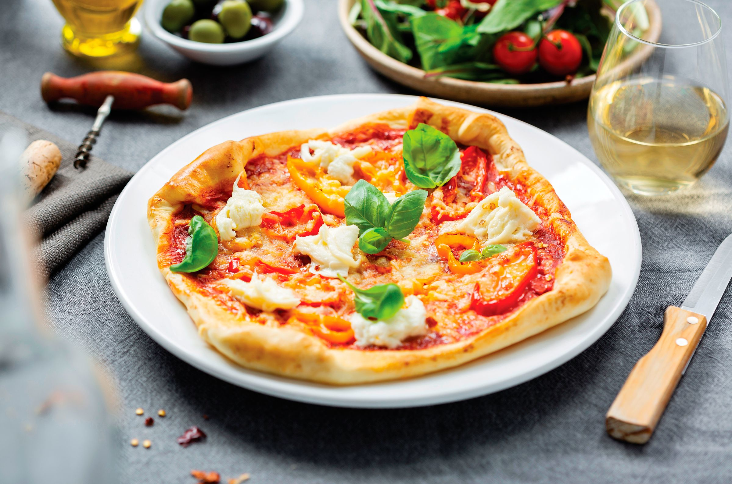 Pizza sur une assiette blanche avec du basilic, des tomates et un verre de vin.