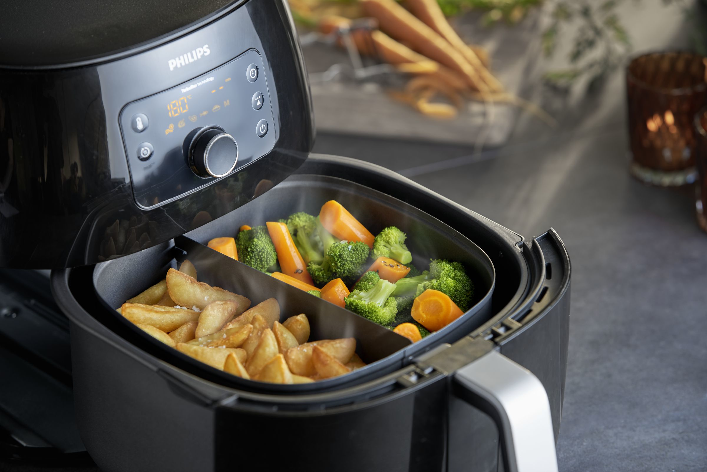 A black Philips air fryer with cooked fries and vegetables inside.