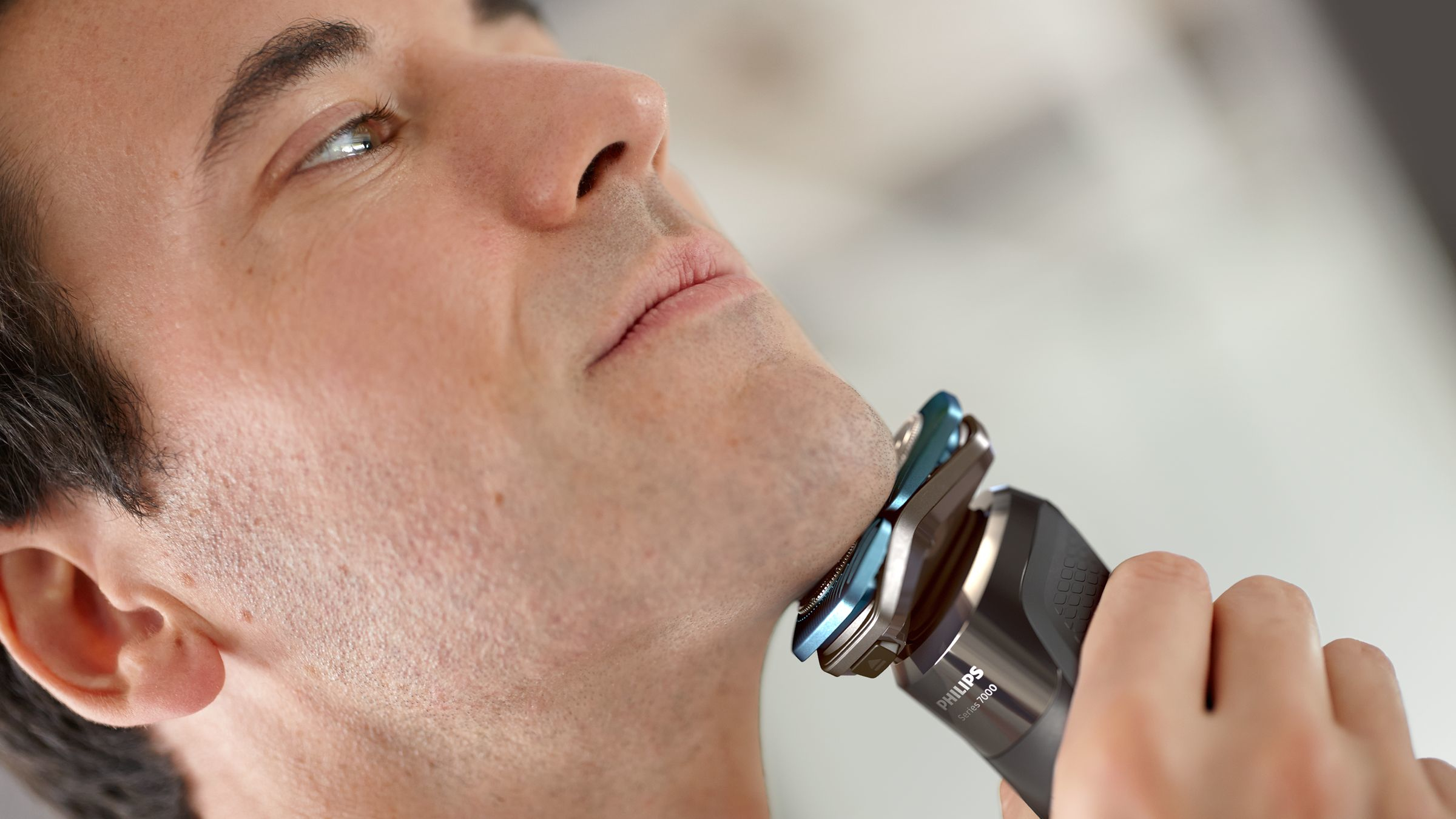 A man is shaving his face with an electric shaver. The shaver is black and silver.