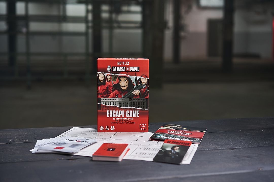 Een Money Heist escape game box set ligt op een tafel met kaarten en instructies. De doos toont personages in rode overalls en maskers.