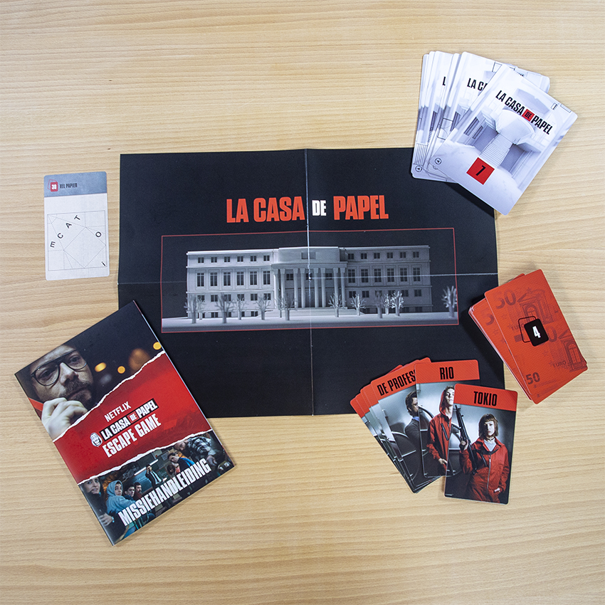 Een 'La Casa de Papel' escape game set op een houten oppervlak. Bevat kaarten, een boekje en een bordspel element met een gebouw afbeelding.