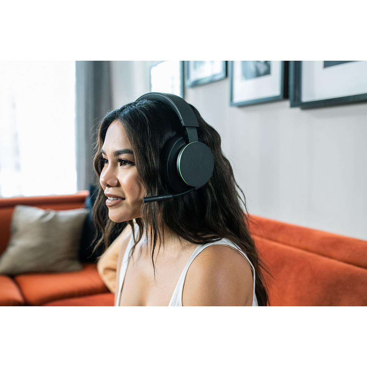 Frau mit schwarzem Headset, die auf einem orangenen Sofa sitzt.
