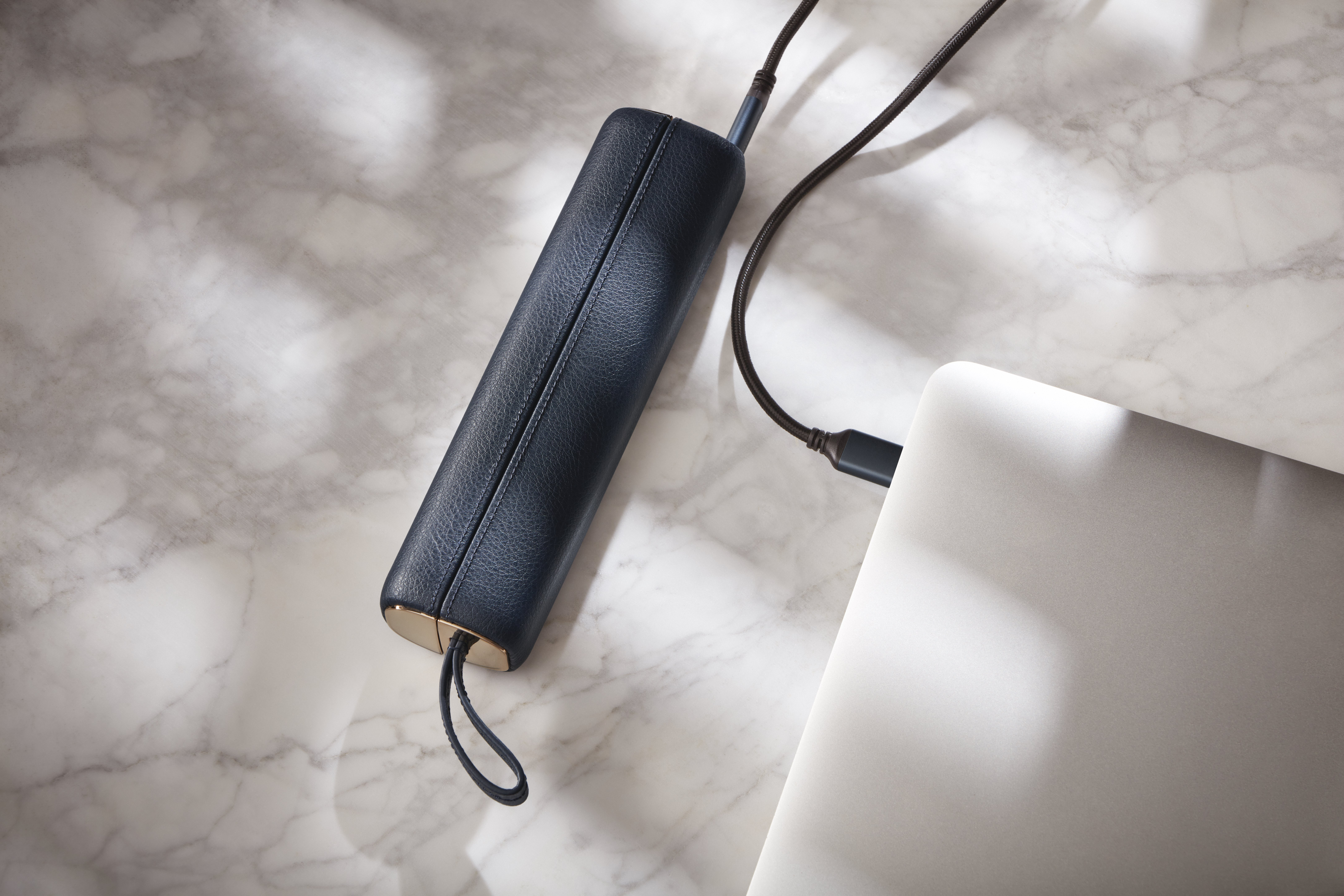 Laptop mit Kabel und dunkelblauer Lederhülle.
