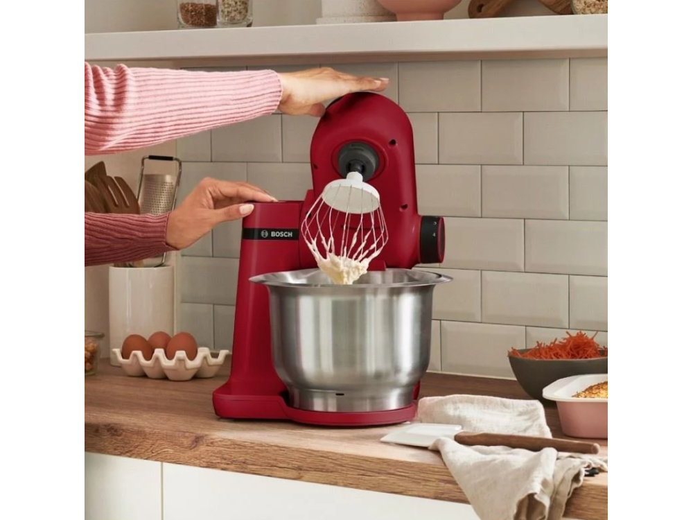 Batidora de cocina roja, con batidor blanco en un cuenco plateado. Superficie de madera y mano.