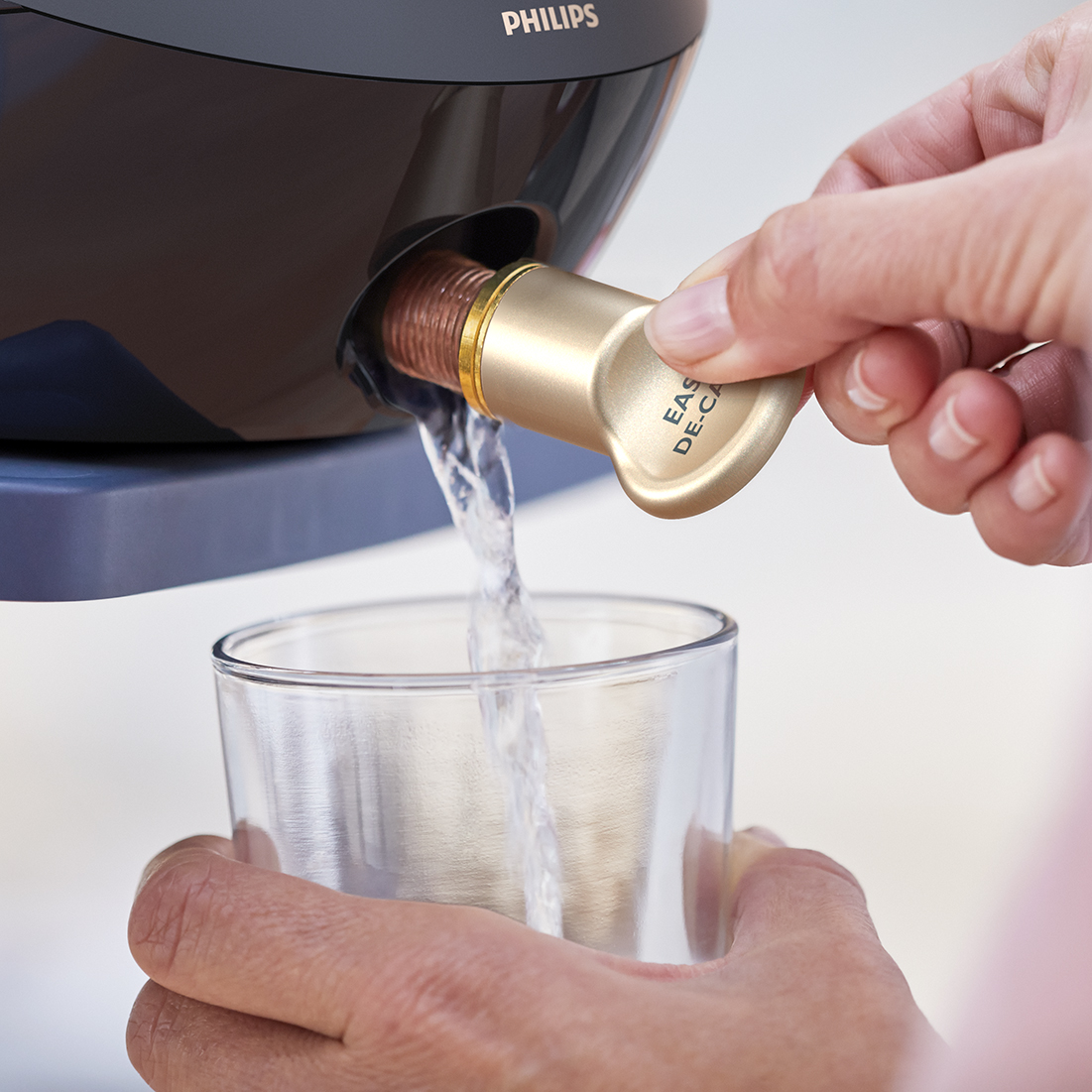 Wasser fließt aus einem goldenen Wasserhahn in ein Glas. Hände, Philips-Branding. Transparenter Hintergrund.