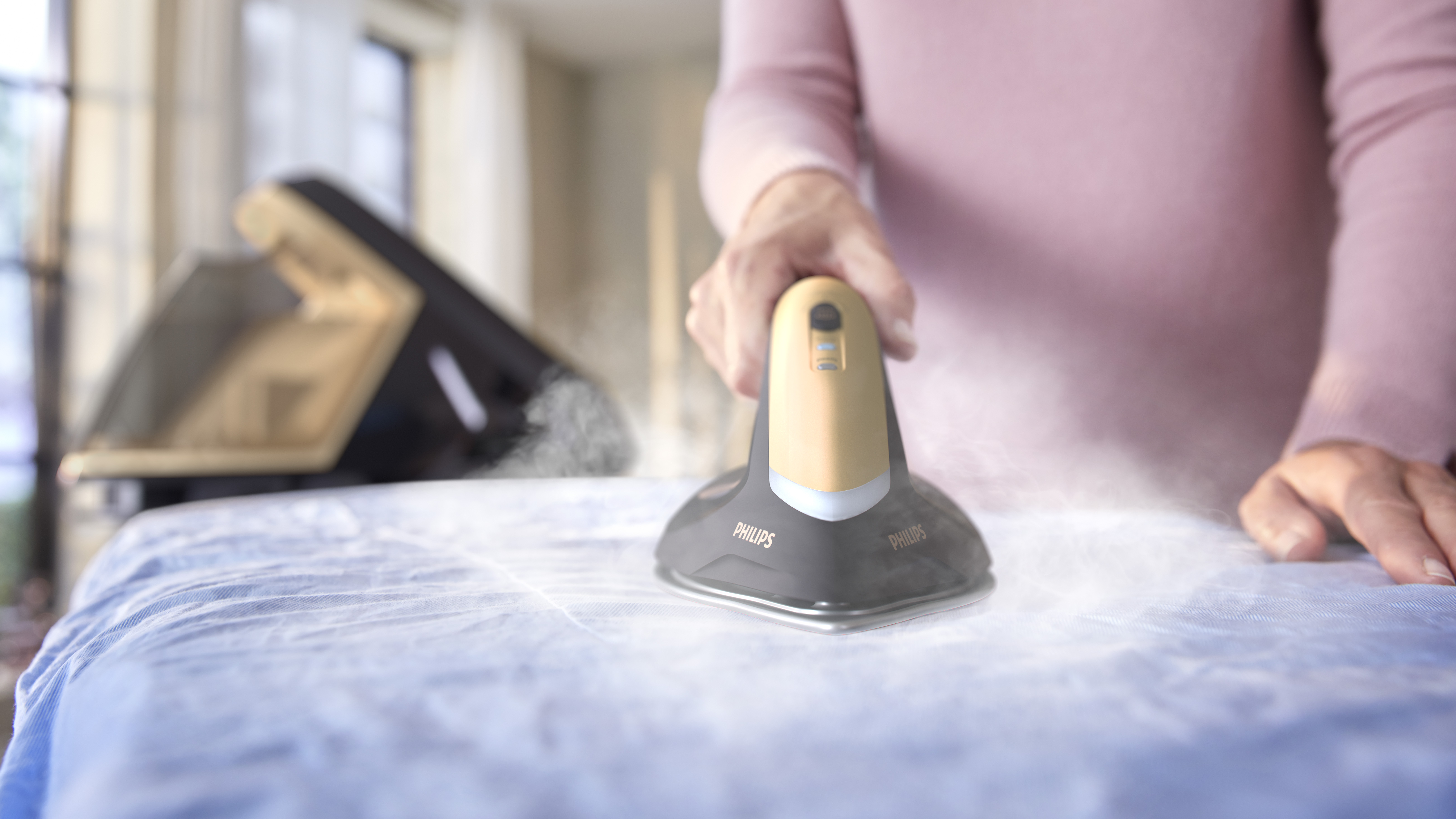 Eine Person bügelt ein blaues Hemd mit einem Philips Bügeleisen, Dampf ist sichtbar.
