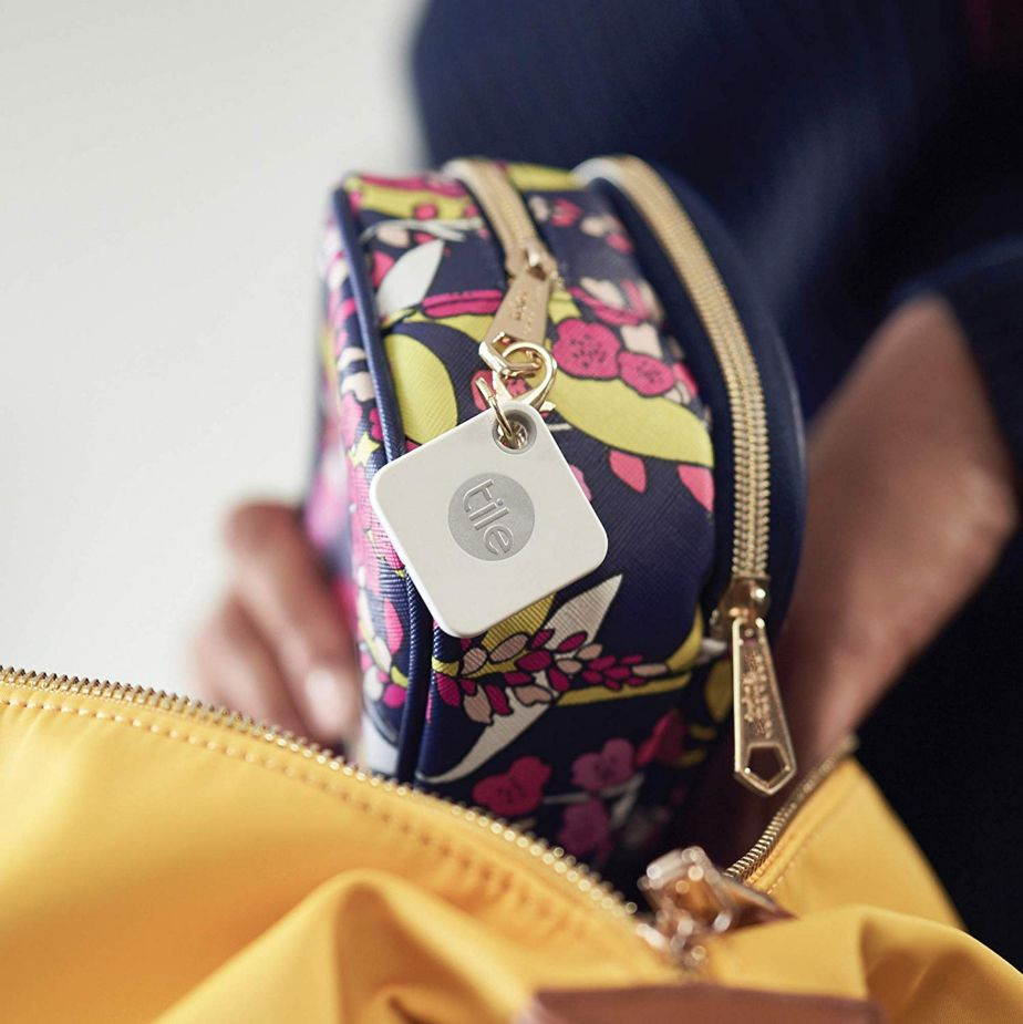 A white Tile tracker on a bag with a floral print, with a yellow bag in the background.