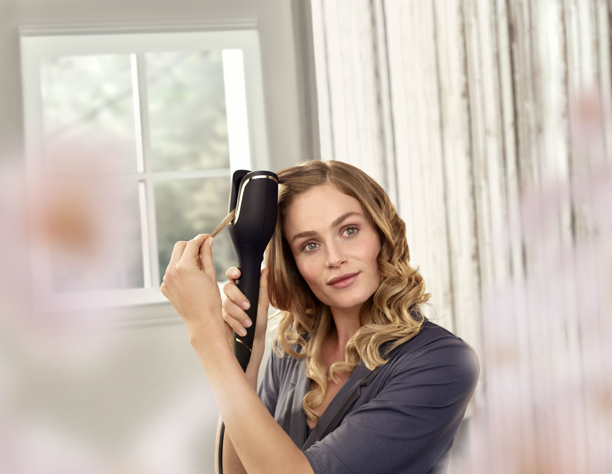 Woman using a curling iron. She holds a strand of hair and looks at the camera.