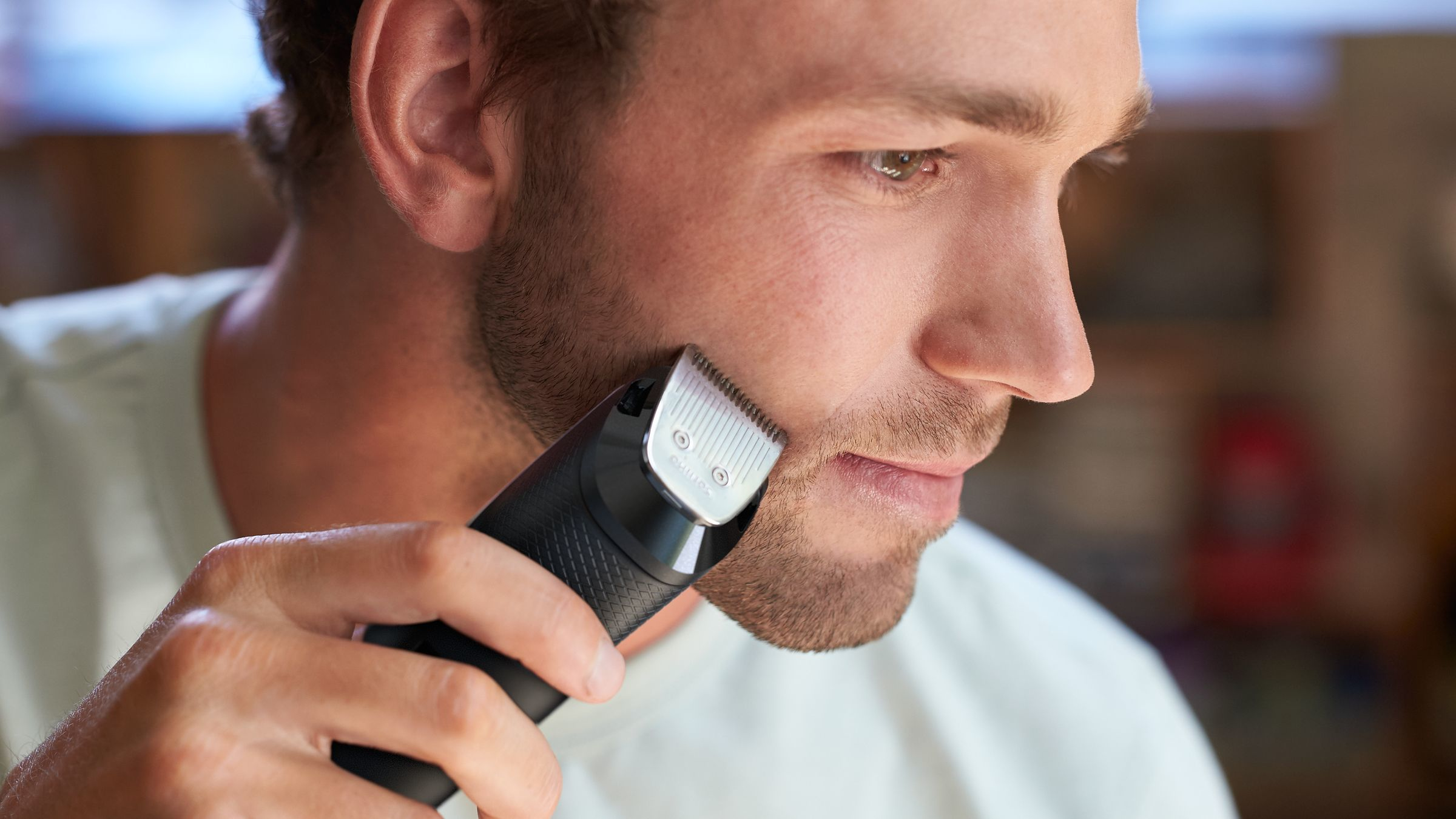 Een man scheert zijn baard met een elektrische trimmer. De trimmer is zwart en zilver. De man heeft een lichte huid en bruin haar.