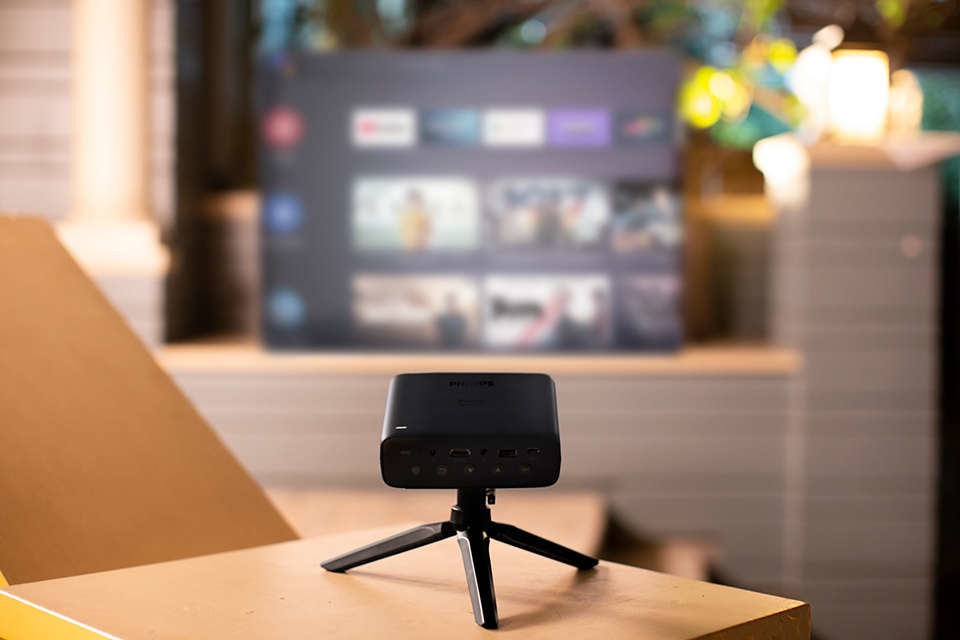 Een zwarte Philips projector op een statief, met een wazig scherm.
