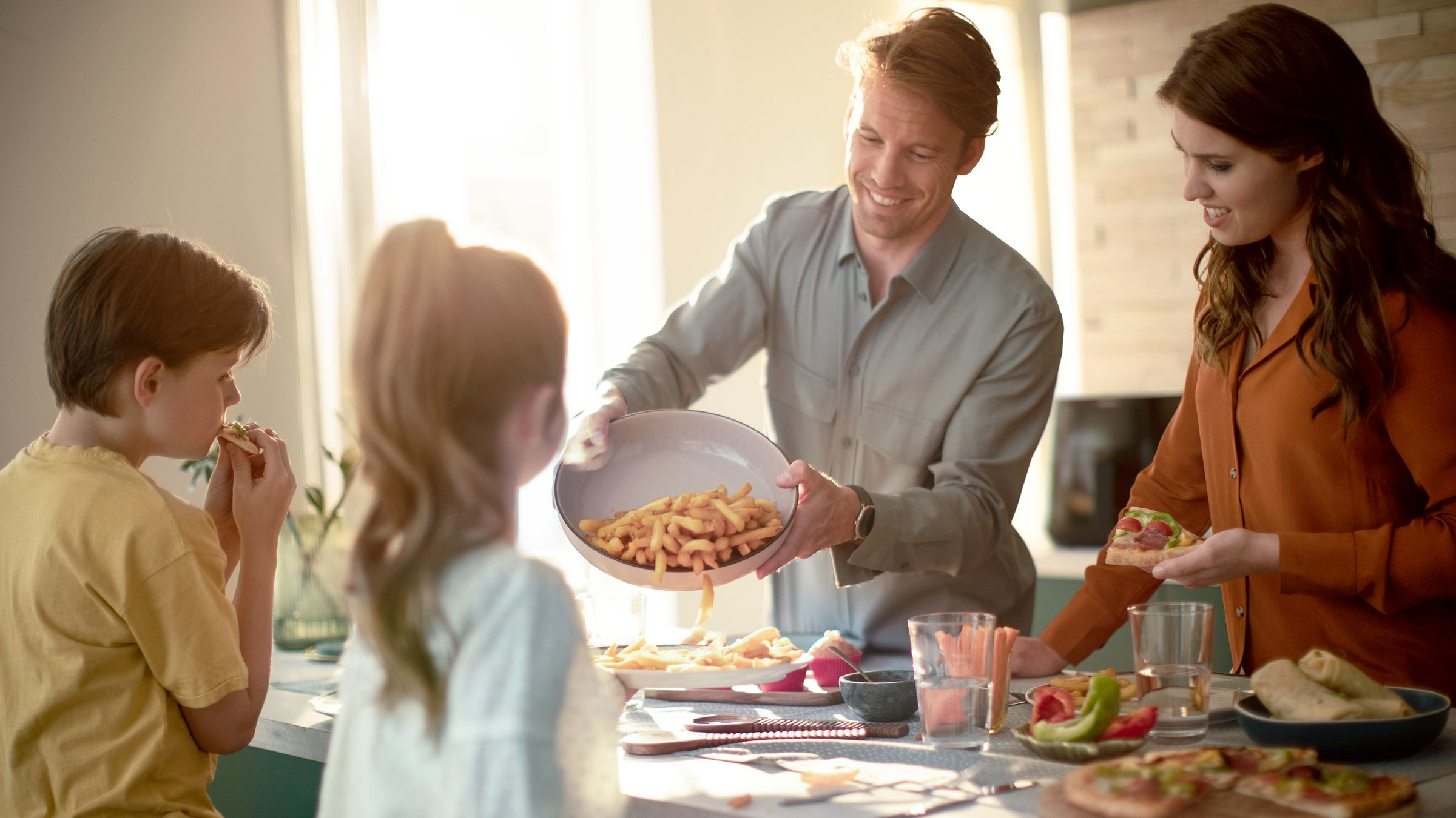 Une famille mange ensemble, le père sert des frites aux enfants.