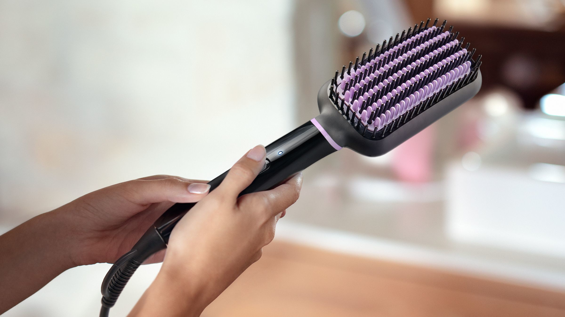Hands holding a black hair straightening brush with pink bristles.