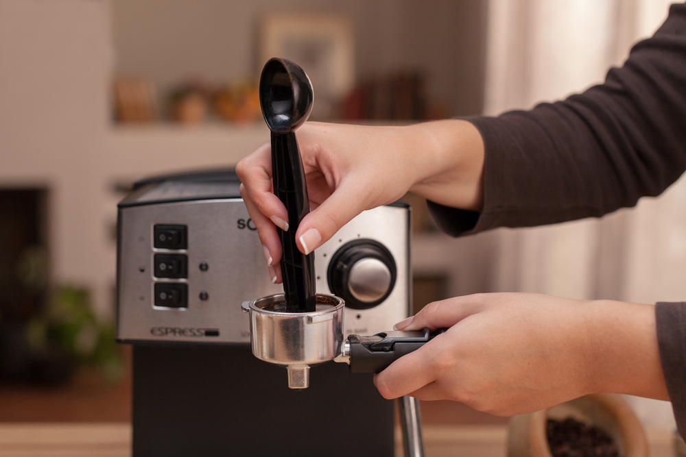 Una persona llena un portafiltro con café molido usando una cuchara, máquina de espresso.