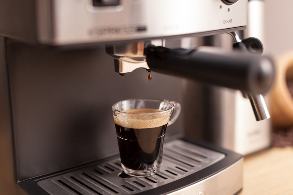 Máquina de espresso con taza de vidrio. El café gotea en la taza. Mesa de madera.