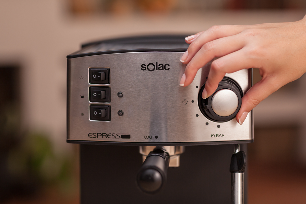 Una mano gira un dial plateado en una máquina de espresso de acero inoxidable.