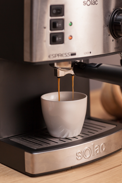 Máquina de café dispensando espresso. Una taza blanca está bajo el surtidor, y el café fluye.