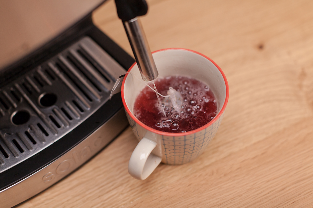 Máquina de espresso vertiendo té en taza estampada sobre superficie madera.