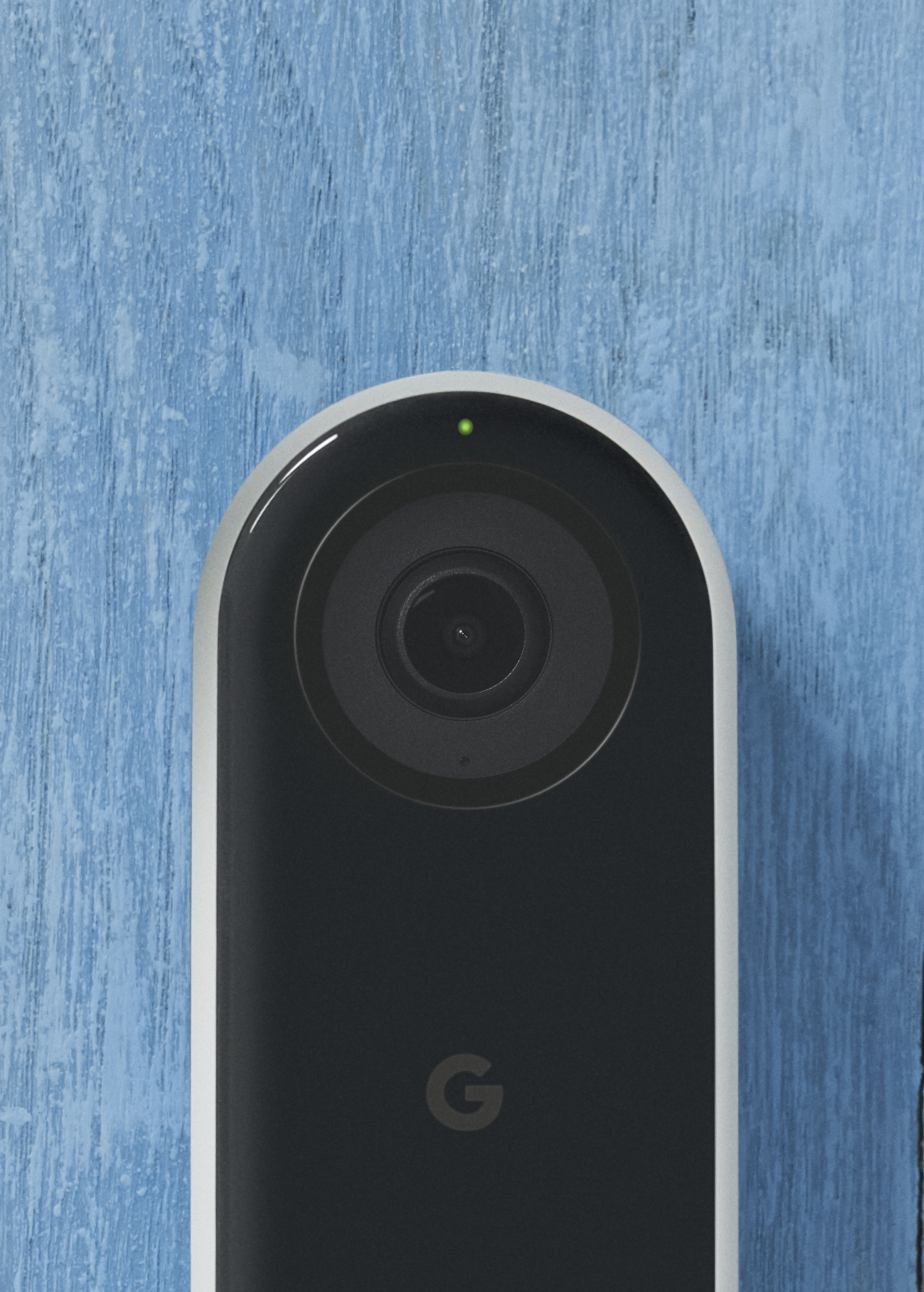 Schwarze und weiße Google Nest Türklingel auf blauer Holzoberfläche. Ein grünes Licht sichtbar.
